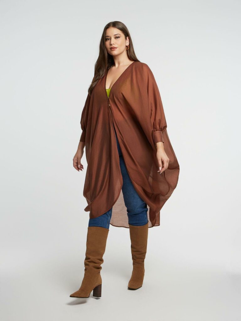 Plus size μοντέλο ποζάρει με καφέ αέρινο φόρεμα τουνίκ με μπαλούν μανίκια.
