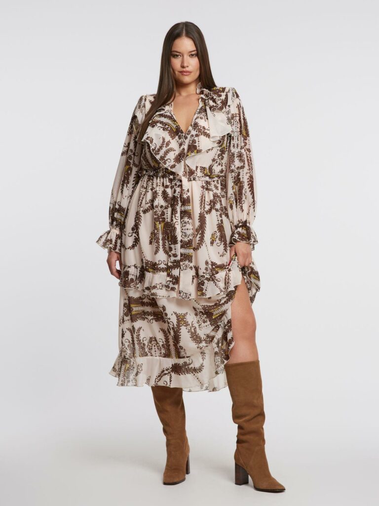 Plus size μοντέλο ποζάρει με καφέ midi φόρεμα με βολάν και paisley μοτίβο.