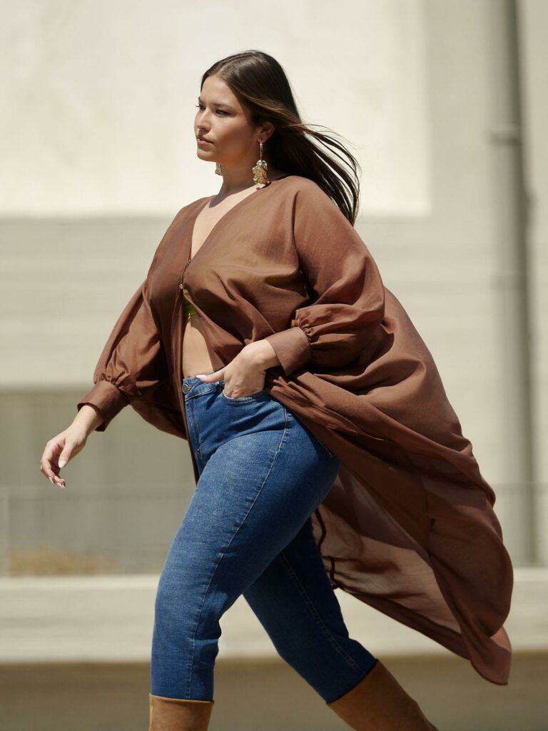 Plus size trends για το 2025: Plus size μοντέλο ποζάρει φορώντας ένα σοκολατί αέρινο φόρεμα τουνίκ με μπαλούν μανίκια.